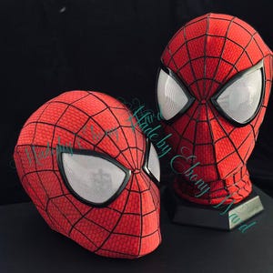 May include: Two red and black Spider-Man masks with white eye lenses. The masks have a web pattern and are displayed on a black surface. The text "Made by Ebony Nur" is visible.