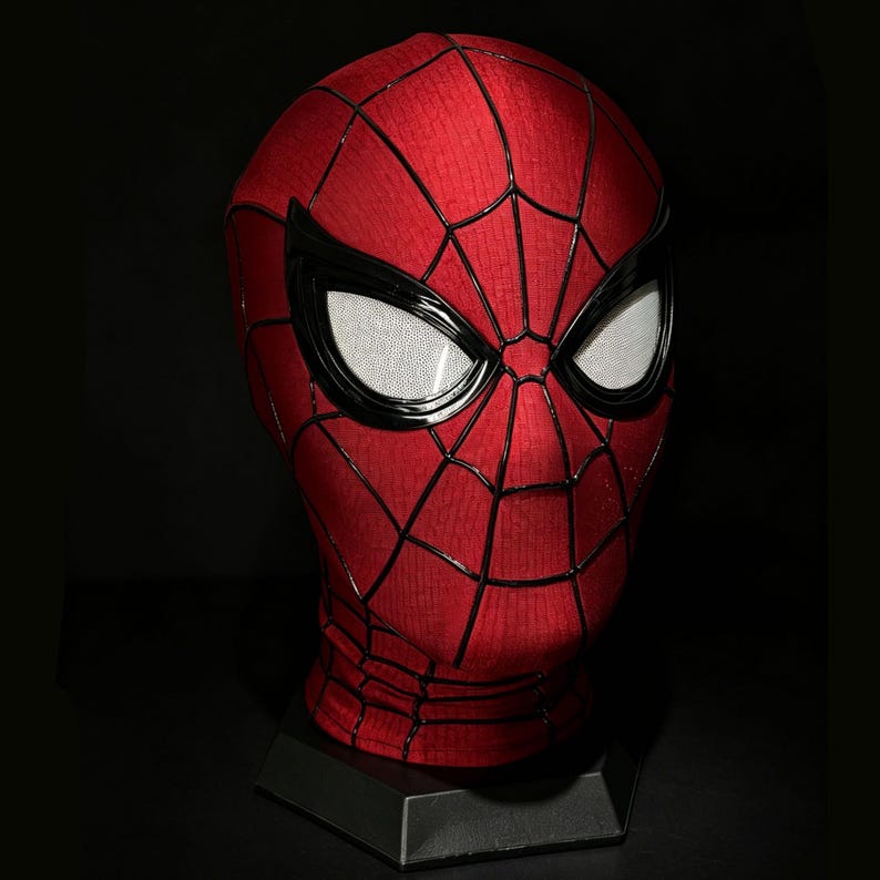 以下が含まれることがあります： 赤と黒のスパイダーマンマスク、白いレンズ付き。マスクはクモの巣模様で、黒い台座に展示されています。レンズはテクスチャ加工されています。