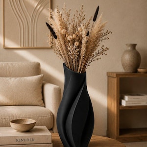 May include: A matte black vase with a spiraling, twisted silhouette, filled with a tall arrangement of dried beige grasses, small light-colored flowers, and several dark brown, slender, fuzzy-tipped botanical stems.