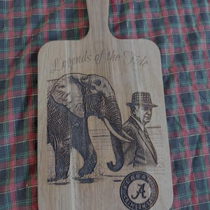 May include: Wooden cutting board with a handle, engraved with an elephant, a man in a suit, and the words "Legends of the Tide." The board also features a circular emblem with the letter "A" and the words "Crimson Tide."