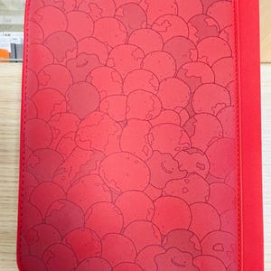 Może przedstawiać: Czerwona okładka notatnika z powtarzającym się wzorem kul w stylu kreskówkowym. Kule mają ciemniejszy czerwony kontur i uśmiechniętą twarz. Okładka ma jednolity czerwony grzbiet i szytą obwódkę.