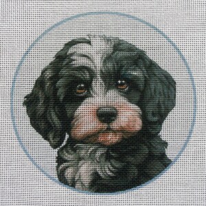 May include: A needlepoint canvas featuring a portrait of a dog. The dog has black and white fur, with brown eyes and a pink nose. The dog is framed by a light blue oval on a white background.