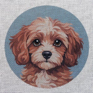 May include: A needlepoint canvas featuring a Cavalier King Charles Spaniel dog. The dog has brown and white fur, large brown eyes, and a black nose. The dog is set against a light blue oval background.