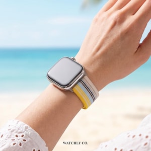 May include: A silver smartwatch with a rectangular screen and a fabric watch band featuring horizontal stripes in yellow, light blue, white, and dark brown. The watch band has a woven texture and is secured with a metal buckle mechanism.