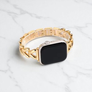 May include: A gold-colored chain link watch band with a silver watch face. The band is made of interlocking links and is designed to fit a smartwatch. The watch face has a black screen.