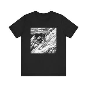 May include: Black t-shirt featuring a square graphic of a dinosaur skeleton skiing down a snowy mountain. The black and white illustration shows the dinosaur on skis, with a mountain range and cloudy sky in the background.