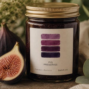 Può includere: Un barattolo di confettura di fichi con coperchio dorato ed etichetta con campioni di colore viola. L'etichetta recita "FIG PRESERVES Summer Harvest batch 01". Un fico a fette e un fico intero sono in primo piano.