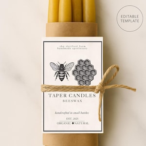 Könnte beinhalten: Ein Bündel gelber Bienenwachs-Taperkerzen, mit Bindfaden gebunden. Das Etikett zeigt eine Bienen- und Wabenillustration mit dem Text "TAPER CANDLES BEESWAX" und "handcrafted in small batches". Das Etikett enthält auch den Text "ORGANIC NATURAL".