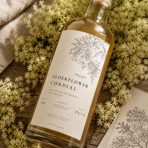 Könnte beinhalten: Eine klare Glasflasche mit Holzkorken, gefüllt mit Holunderblüten-Cordial. Das Etikett zeigt eine botanische Illustration und den Text "Elderflower Cordial". Die Flasche enthält 236 ml Flüssigkeit.