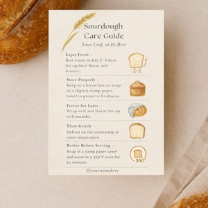 Może przedstawiać: Kremowa karta zatytułowana "Sourdough Care Guide" z instrukcjami dotyczącymi przechowywania, zamrażania i odświeżania chleba na zakwasie. Karta zawiera ilustracje chleba i kłosa pszenicy. Tekst zawiera "Enjoy Fresh" i "Revive Before Serving".