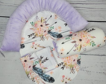 May include: A baby nest with a floral and arrow print. The nest is made of soft fabric and has a purple plush border. It includes a matching pillow with a floral and arrow print.