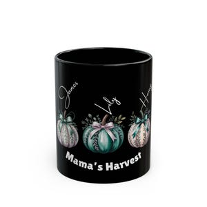 May include: Black ceramic mug featuring three watercolor pumpkins with names James, Lily, and Henry. The pumpkins are teal, green, and pink with bows and foliage. The text "Mama's Harvest" is printed below the pumpkins.