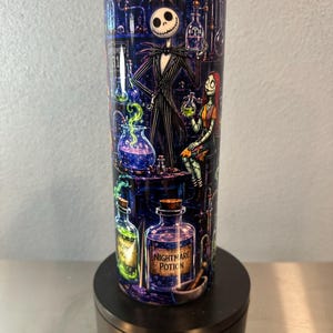 May include: A cylindrical tumbler featuring a dark, laboratory-themed graphic with Jack Skellington and Sally. The design includes various glass potion bottles, one labeled Nightmare Potion, glowing green and purple liquids, and a spiderweb.