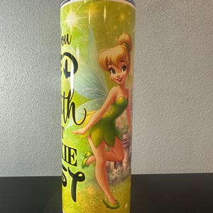 May include: A stainless steel tumbler featuring a cartoon image of Tinkerbell in a green dress with wings. The tumbler has a green and yellow background with the text "You can fly with faith, trust, and pixie dust."