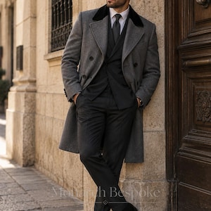 May include: A charcoal grey double-breasted wool overcoat with a black velvet collar, worn over a dark grey suit consisting of a vest, trousers, and a white dress shirt with a dark tie. The ensemble includes black leather dress shoes and sunglasses.