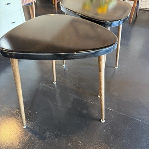 May include: Two vintage black triangular side tables with light wood legs. The tables have a mid-century modern design, with a sleek, minimalist aesthetic. The tables are likely made of wood and metal.