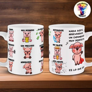 May include: White ceramic mug featuring cartoon pigs with various labels in Spanish. The mug has a handle and is decorated with colorful illustrations and text, including "MUY HERMOSO" and "ES LO QUE SOY". The mug has a glossy finish.