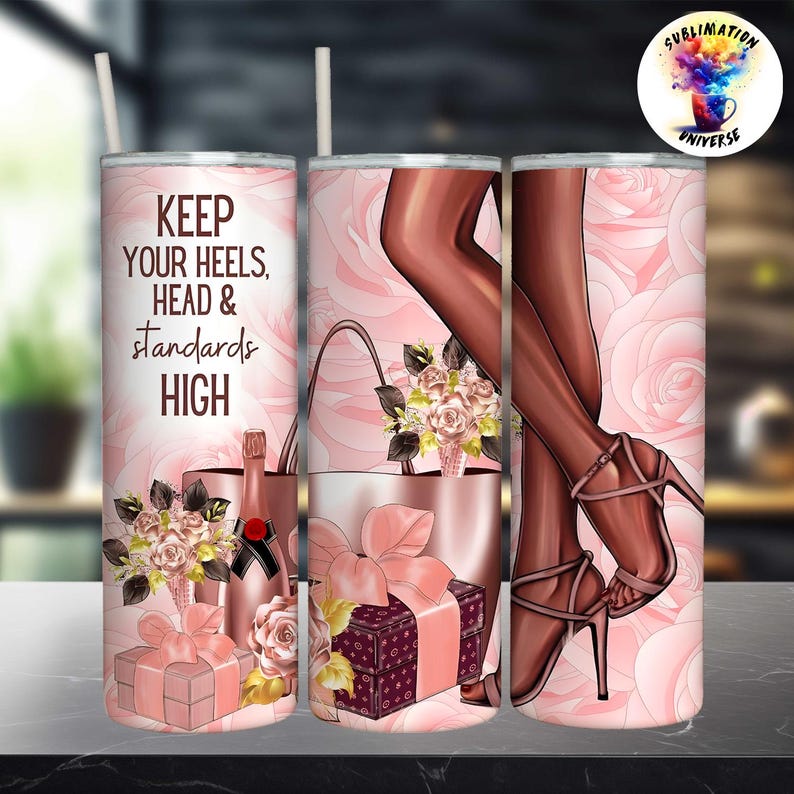 May include: A pink tumbler with a floral and high heels design. The tumbler features the text "KEEP YOUR HEELS, HEAD & STANDARDS HIGH". The design includes a champagne bottle, gifts, and a purse.