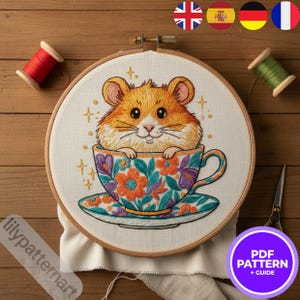 Peut inclure: Broderie représentant un hamster dans une tasse à fleurs. La tasse est ornée de fleurs orange, violettes et turquoise. Le texte "PDF PATTERN + GUIDE" est dans un cercle violet. Comprend des bobines de fil.