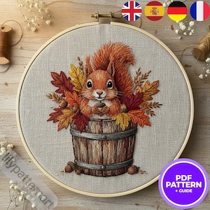 Peut inclure: Broderie sur toile représentant un écureuil roux tenant une noix, entouré de feuilles d'automne, dans un tonneau en bois. Le tout est encadré dans un cercle en bois. Le texte "PDF PATTERN + GUIDE" est dans un cercle violet.