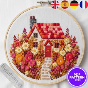 Peut inclure: Broderie d'une scène de cottage dans un cercle en bois. Le cottage a un toit rouge, une porte rouge avec un cœur et est entouré de fleurs colorées. Le texte "lilypatternart" est en bas à gauche. Un cercle violet avec le texte "PDF PATTERN + GUIDE" est en bas à droite.