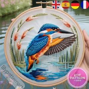 May include: An embroidered artwork in a wooden hoop, depicting a kingfisher bird with blue, orange, and black feathers. The design includes water and reeds, with the text "lilypatternart" and "PDF PATTERN + GUIDE".
