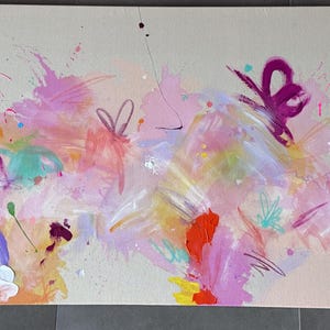 May include: A rectangular canvas painting featuring an abstract composition with a light beige background. The artwork displays vibrant splashes and brushstrokes of pink, magenta, orange, yellow, light blue, and purple paint across the surface.