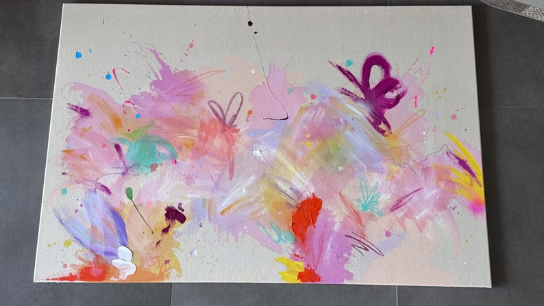 May include: A rectangular canvas painting featuring an abstract composition with a light beige background. The artwork displays vibrant splashes and brushstrokes of pink, magenta, orange, yellow, light blue, and purple paint across the surface.