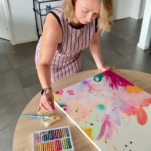 May include: A sleeveless pink dress with black vertical stripes, a rectangular canvas featuring abstract pink, orange, and green paint splatters, a two-tier box of colorful oil pastels, a tube of magenta acrylic paint, and a pink paint bottle.