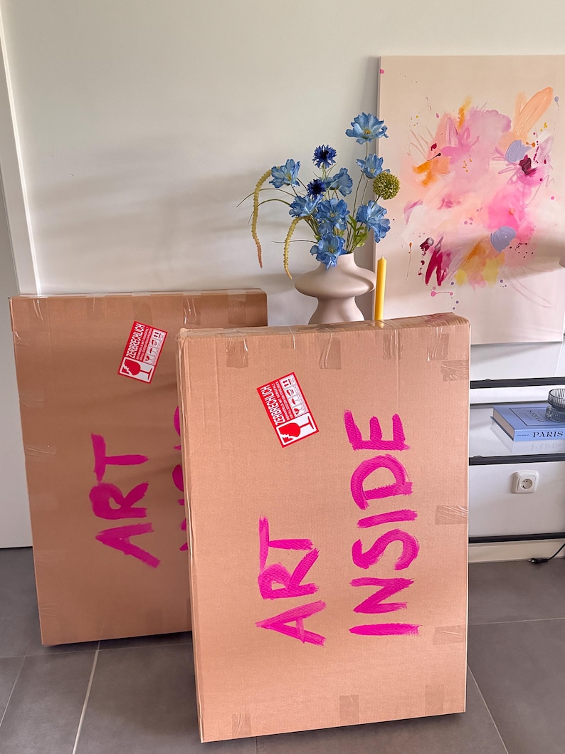 May include: Two large rectangular cardboard shipping boxes with the words ART INSIDE written in bright pink paint. Each box features a red and white fragile sticker with the German text ZERBRECHLICH. The boxes are sealed with clear tape.