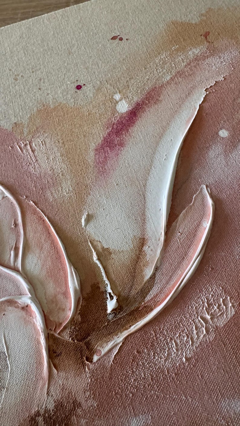 May include: A textured canvas painting featuring abstract shapes in shades of beige, cream, and dusty rose. Thick, raised white and light pink paint strokes create organic forms, accented by small splatters of deep magenta and brown paint.