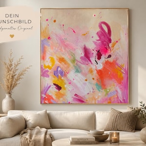 May include: A square abstract painting in a thin gold frame featuring vibrant splashes of hot pink, orange, yellow, and purple paint on a light beige background. The artwork displays energetic brushstrokes and splatters of color throughout.