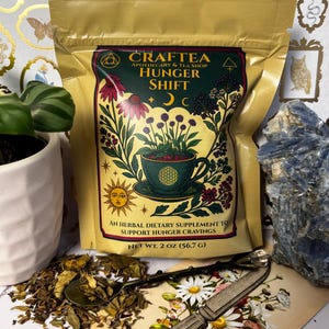 Peut inclure: Un sachet doré de "CRAFTEA HUNGER SHIFT", un complément alimentaire à base de plantes. L'étiquette présente une tasse à thé avec des fleurs et le texte "AN HERBAL DIETARY SUPPLEMENT TO SUPPORT HUNGER CRAVINGS". Le poids net est de 56,7 grammes.