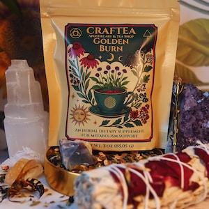 May include: A beige pouch of "CRAFTEA GOLDEN BURN" herbal tea, with a floral illustration of a teacup and flowers. The package is labeled as an herbal dietary supplement for metabolism support. The image includes a selenite tower, crystals, and a bundle of sage.