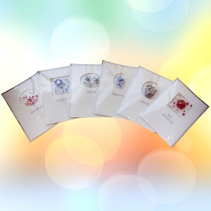 May include: A collection of white greeting cards with various designs. Some cards feature embedded decorative elements like flowers and hearts. Text on the cards includes "Happy Birthday," "Get Well Soon," "Thank You," and "Happy Valentine's Day."