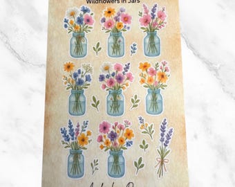 May include: A sticker sheet featuring illustrations of wildflowers in mason jars. The jars are filled with colorful blooms in shades of pink, yellow, blue, and purple. The text "Wildflowers in Jars" is at the top, and the Avalon Lane Designs logo and website are at the bottom.