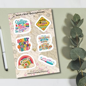May include: A sticker sheet titled Stitch & Bitch Quilting Stickers featuring six colorful designs with quilting themes, including text like Quilting is my Love Language, Warning This Vehicle Stops at all Quilt Shops, and As ye sew, so shall ye rip.