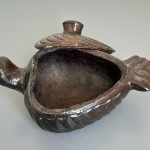 Peut inclure: Une boîte à bijoux en céramique brun foncé en forme de poisson avec un dessus ouvert. Le couvercle est détaché et repose partiellement sur l'ouverture, avec une petite poignée en bouton. Le corps du poisson présente une texture nervurée.