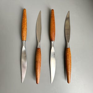 May include: Four knives with tapered stainless steel blades and cylindrical wooden handles. Each blade features a pointed tip and a smooth edge, with the word BIRKS engraved near the bolster. The wooden handles have a visible grain pattern.