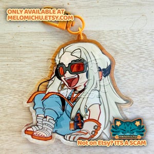 May include: A clear acrylic charm featuring a cartoon character with white hair, red-tinted glasses, and blue clothing. The charm has an orange clasp and the text "ONLY AVAILABLE AT MELOMICHU.ETSY.COM" and "Not on Etsy? ITS A SCAM".