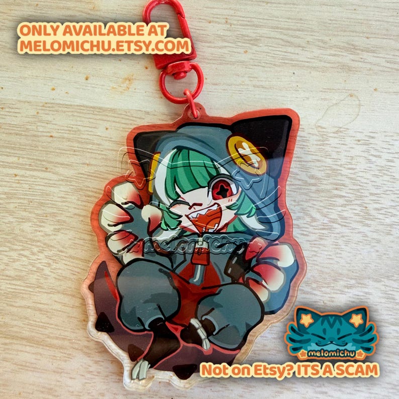 May include: A clear acrylic charm featuring a cartoon character with green hair, a red eye, and a gray hoodie. The charm has a red lobster clasp. Text on the charm reads "ONLY AVAILABLE AT melomichu.etsy.com" and "Not on Etsy? ITS A SCAM".