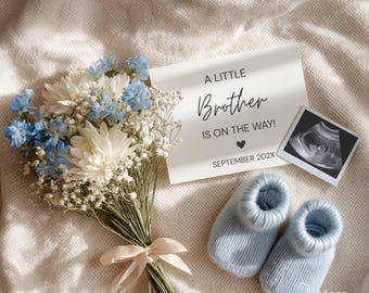 Peut inclure: Annonce de grossesse avec un bouquet de fleurs blanches et bleues, une carte avec l'inscription "A Little Brother Is On The Way !" et une échographie. Deux chaussons bleus clairs sont également présents.