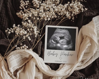 May include: A sonogram image of a baby, with the text "Baby Parker" and "February 202X" printed on a white card. The card is surrounded by white flowers and draped fabric in shades of brown and cream.