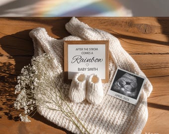 Peut inclure: Une couverture en tricot crème avec une pancarte en bois indiquant "AFTER THE STORM COMES A Rainbow BABY SMITH", des chaussons pour bébé et une échographie. Un arc-en-ciel est visible en arrière-plan, sur une surface en bois.