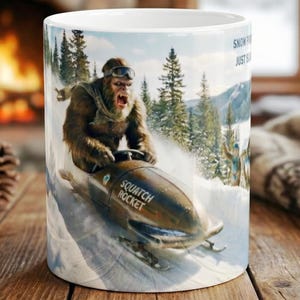 May include: White ceramic mug featuring a vintage illustration of Bigfoot riding a snowmobile down a snowy mountain. The snowmobile is labeled "Squatch Rocket". The mug has the text "Snow Fun, Just Sayin".