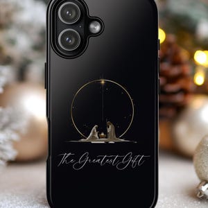 May include: Black phone case featuring a gold circular design with a Nativity scene and the text "The Greatest Gift." The case has a glossy finish and a dual-camera setup.