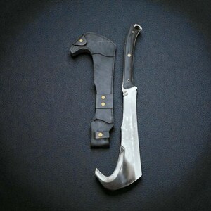 Könnte beinhalten: Ein Messer mit gebogener Klinge, Holzgriff und schwarzer Lederscheide. Die Klinge ist silberfarben und der Griff dunkel mit Messingnieten. Die Scheide ist aus schwarzem Leder mit Messingknöpfen. Das Messer ist zum Schneiden bestimmt.