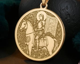 May include: Gold-colored pendant necklace featuring a detailed relief of a person on horseback, holding a flag. The round pendant hangs from a delicate chain. The design is set against a dark green velvet background.