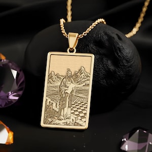May include: A gold-colored pendant necklace featuring a rectangular pendant with an engraved image of a person in a landscape. The necklace is displayed on a black surface with several faceted gemstones in shades of purple and orange.