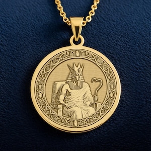 Op de afbeelding: Goudkleurige hangerketting met een gedetailleerde gravure van een Egyptische farao. De ronde hanger hangt aan een fijne ketting. De farao zit, draagt een kroon en houdt een staf vast. De achtergrond is diepblauw.